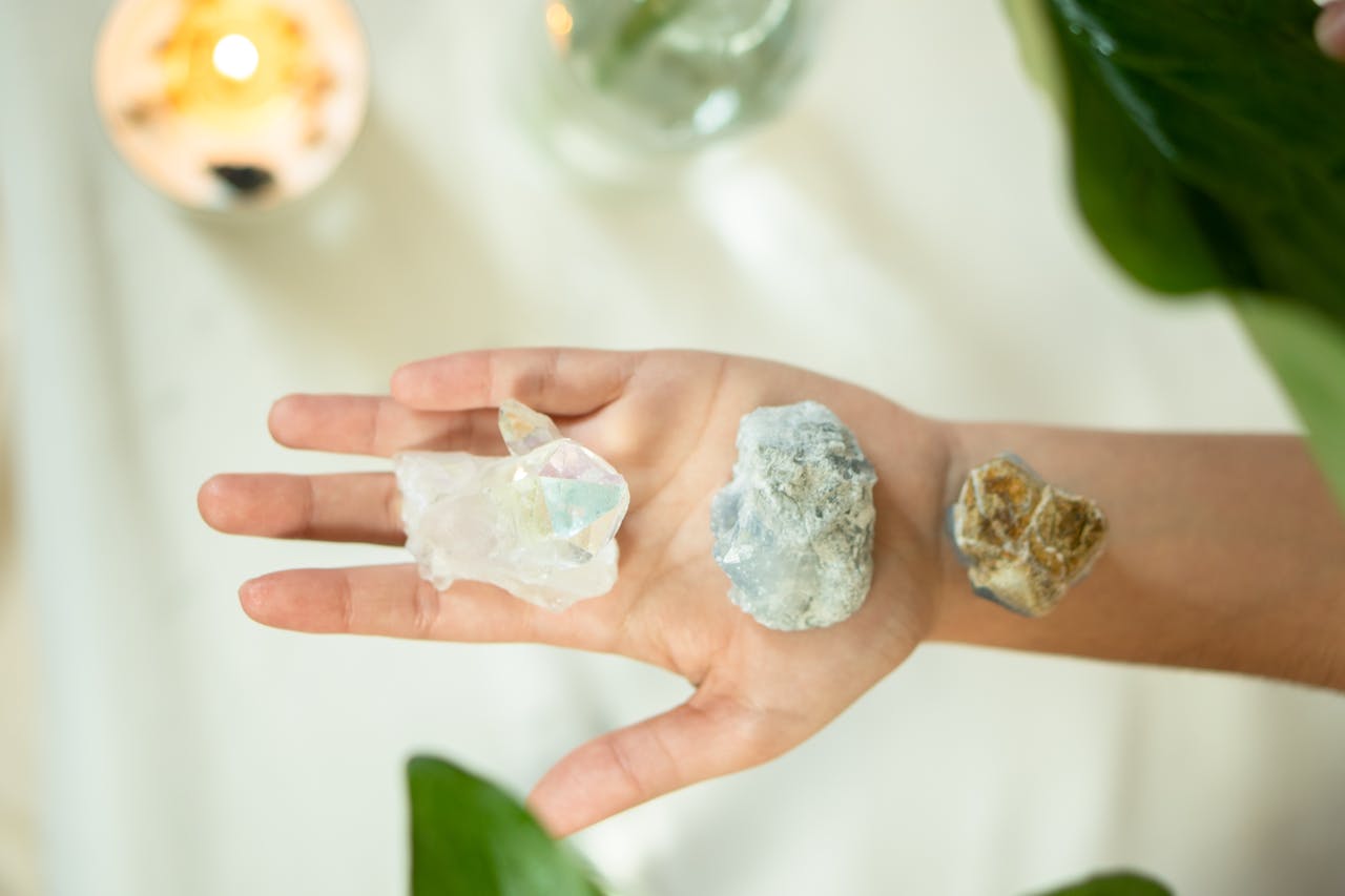 Overhead shot of a hand holding three crystals, surrounded by greenery and a lit candle.