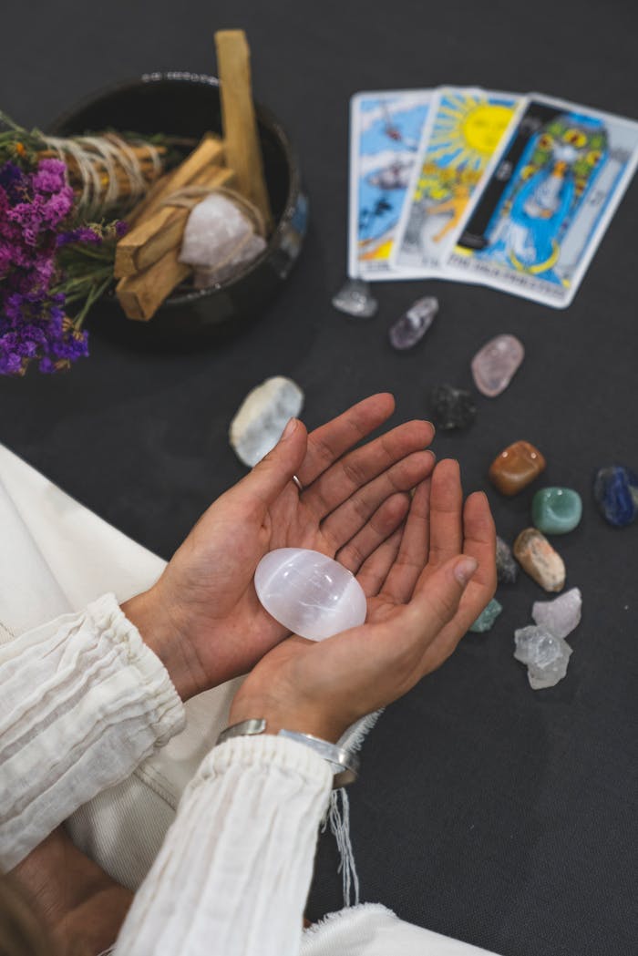 Close-up of hands holding healing stone with tarot cards on surface, promoting spiritual healing.